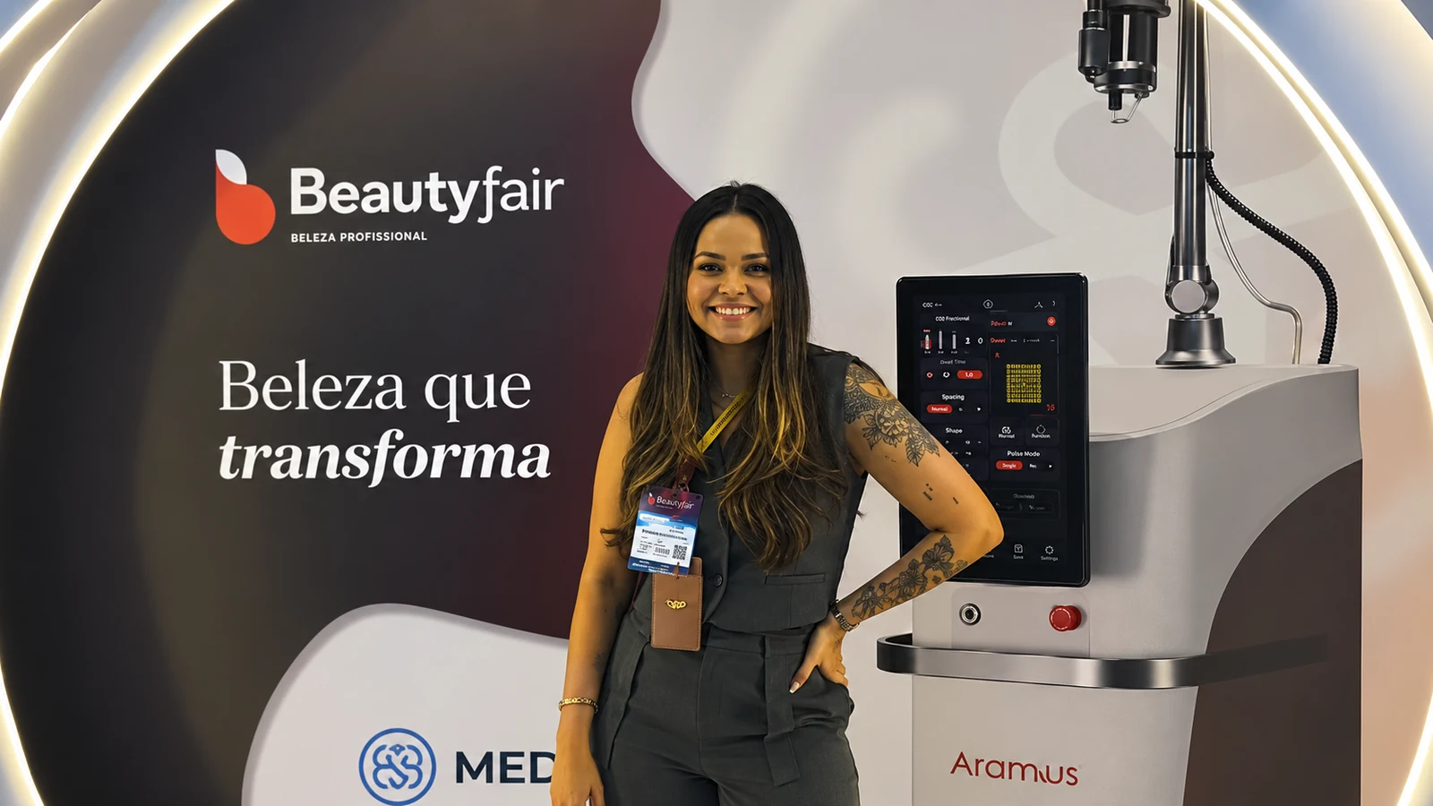 Representante da Cosmética Eventos no estande da Beauty Fair 2026, em São Paulo, ao lado de um equipamento de estética